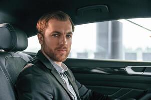 Portrait of man in formal, business clothes that is sitting in the modern automobile photo