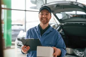With ,box, and ,notepad. Man in blue uniform is working in the car service photo