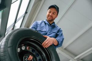 View from, below. Holding tire. Man in blue uniform is working in the car service photo