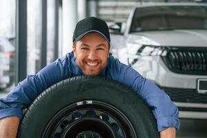 New ,tire.. Leaning on it. Man in blue uniform is working in the car service photo