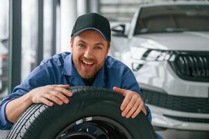 New tire. Leaning on it. Man in blue uniform, is working in the car service photo