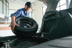 Putting the tire out of automobile... Man in blue uniform is working in the car service photo
