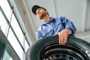 View ,from below., Holding tire. Man in blue uniform is working in the car service photo