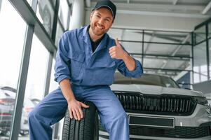 Having fun, smiling,, with tire.. Man in blue uniform is working in the car service photo