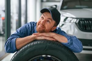 New tire. Leaning ,on it. ,Man in blue uniform is working in the car service photo