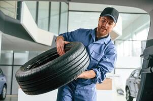 With big new tire for a change. Man in blue ,uniform ,is working in the car service photo