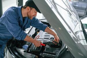 Holding the electrical terminals., Man in, blue uniform is working in the car service photo