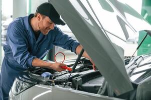 With hood, opened,. Man in blue uniform is working in the car service photo