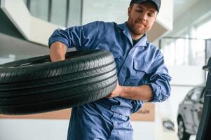 With big ,new, tire for a change. Man in blue uniform is working in the car service photo