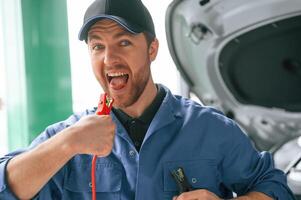 Having fun with electrical terminals,, dangerous. Man in blue uniform is working in the car service photo