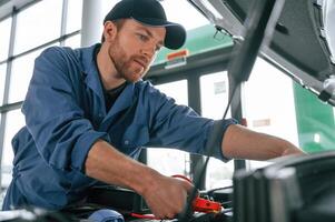 Using the ,electrical, terminals. Man in blue uniform is working in the car service photo