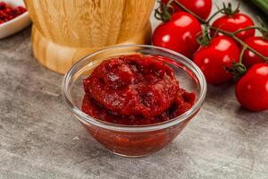 A bowl of tomato sauce next to a knife and a bowl of tomatoes photo