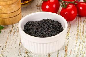 A bowl of black seeds on a table next to tomatoes and herbs photo
