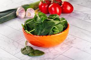 A bowl of spinach on a counter with a knife and a tomato photo