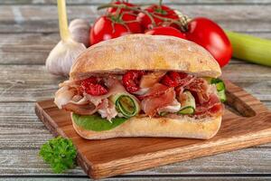 A sandwich with vegetables and meat on a wooden cutting board photo