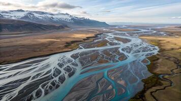 Aerial view of a braided river network flowing through a vast landscape with distant snow capped mountains under a cloudy sky. photo