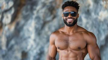 confident man with muscular build smiles in sunglasses against rocky background photo