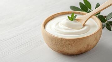 Creamy yogurt in wooden bowl with spoon and green leaves photo