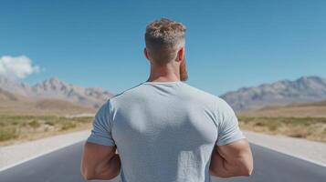 man stands on road, gazing at mountains under clear blue sky photo