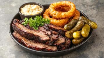 Delicious barbecue meal featuring smoked brisket, onion rings, pickles, and creamy dip photo