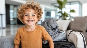 cheerful child with curly hair smiles brightly while sitting next to overstuffed suitcases photo