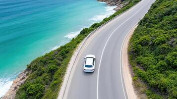 Aerial view of car driving along winding coastal highway beside ocean. vibrant blue water photo