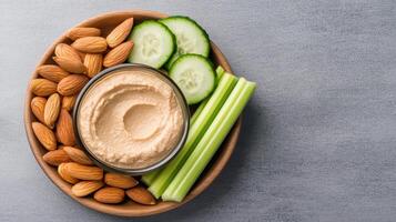Creamy hummus served with fresh cucumber slices, celery sticks, and crunchy almonds creates photo