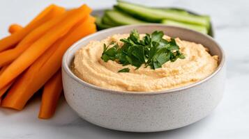 Creamy hummus topped with fresh herbs, served with crunchy carrot and cucumber sticks photo