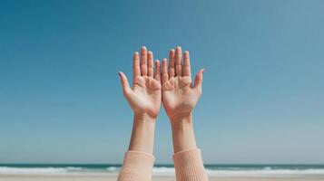 Hands raised towards clear blue sky, expressing freedom and joy at beach photo