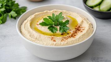 Creamy hummus garnished with olive oil and fresh herbs, served with cucumber slices photo