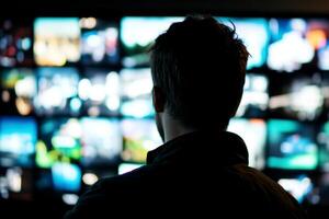 Silhouette of young Caucasian man viewing multiple digital screens in dark room technology concept photo