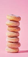 Stack of sugary donuts arranged in a tall tower against a pastel pink background photo
