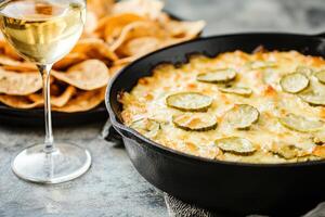 Delicious pickle and cheese dip in cast iron skillet with crispy tortilla chips and wine on rustic table photo