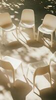 Sunlit circle of white chairs on textured floor under dappled tree shadows, creating a peaceful outdoor setting photo