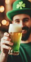 Smiling man holding green beer in a festive hat celebrating st patricks day in a lively pub setting photo