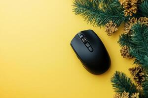 Black computer mouse on yellow background with pine branches creating festive modern tech holiday theme photo