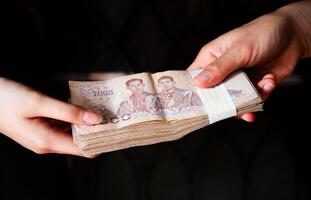Cropped shot view of someone giving pile of Thai baht money to other person. photo