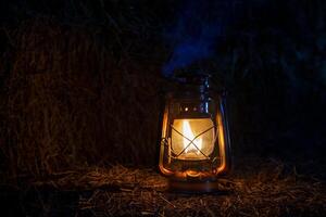 Antique kerosene lantern with light on hay bales in a barn at night photo