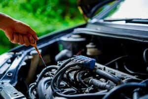 A mechanic holding an oil level gauge in one hand is checking the car's oil level for maintenance, Check your own lubricant level at home photo