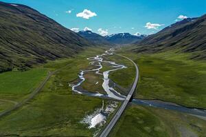 Aerial view of valley road in moss covered landscape near river through ice peak mountains in Iceland in clear day photo