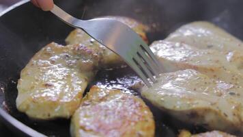 Grilled chicken fillets being flipped with a fork in a pan, sizzling in oil with golden-brown crusts and visible herbs, highlighting the cooking stage video