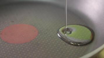 A stream of oil being poured into a non-stick frying pan with a red heat indicator, close-up captures texture and gloss in the early stage of cooking video