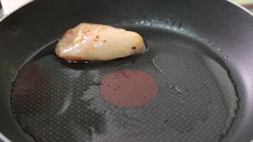 Close-up of hand placing seasoned raw chicken breast into a hot frying pan with oil, capturing a precise moment of cooking initiation and kitchen technique video
