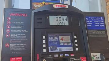 Chicago Illinois 05.03.2025 costco gaz station carburant pompe interface montrant prix et volume, entouré par avertissement panneaux, écran les publicités et accessibilité information dans lumière du jour réglage video