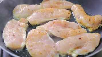 Several seasoned raw chicken fillets sizzling in hot oil on a non-stick pan, close-up captures heat, moisture, and texture at the start of frying video