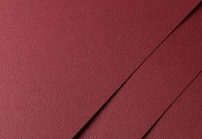 Deep burgundy paper background with a matte texture and fine, tactile surface. Warm red tones create photo