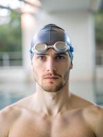 A man wearing a swim cap and goggles is standing in a pool photo
