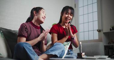 Handheld low angle view shot, Two Asian siblings enjoy birthday celebration together while sitting on the couch in a cozy room at home. Share good times video