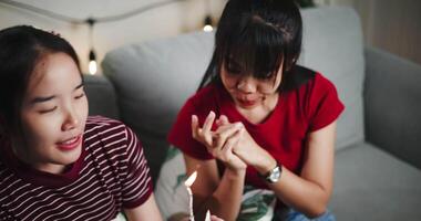 Handheld high angle view shot, Younger Sister gave a small cake to her elder sister and sang a happy birthday song together on the sofa in the cozy room. A happy and warm time of celebration. video