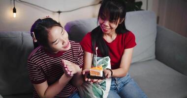 Handheld high angle view shot, The elder sister gave a small cake to her younger sister and sang a happy birthday song together on the sofa in the warm room. A happy and warm time of celebration. video